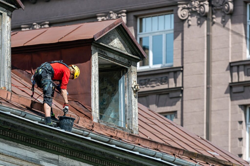 A roofer cleaning clogged gutters