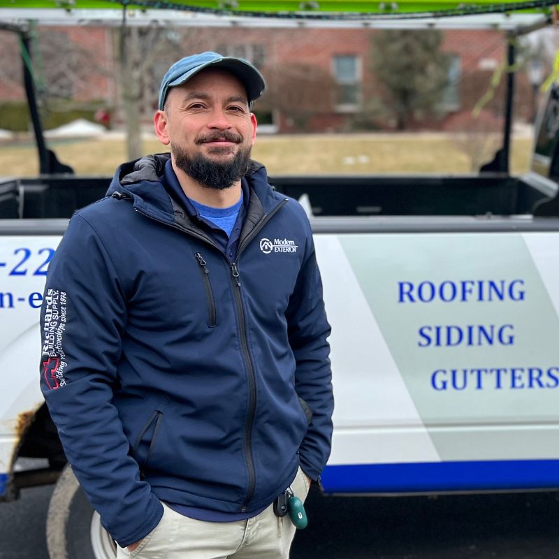 A man standing in front of a truck that says Roofing, siding, gutters.