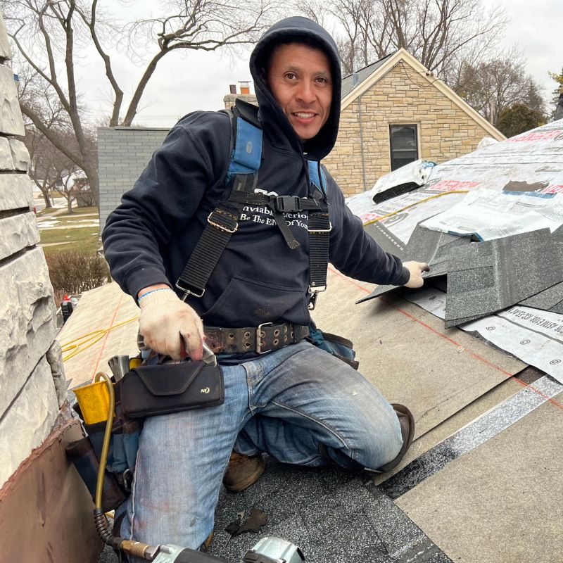 Roofing Crew Member Sitting on roof by chimney about to install Shingles